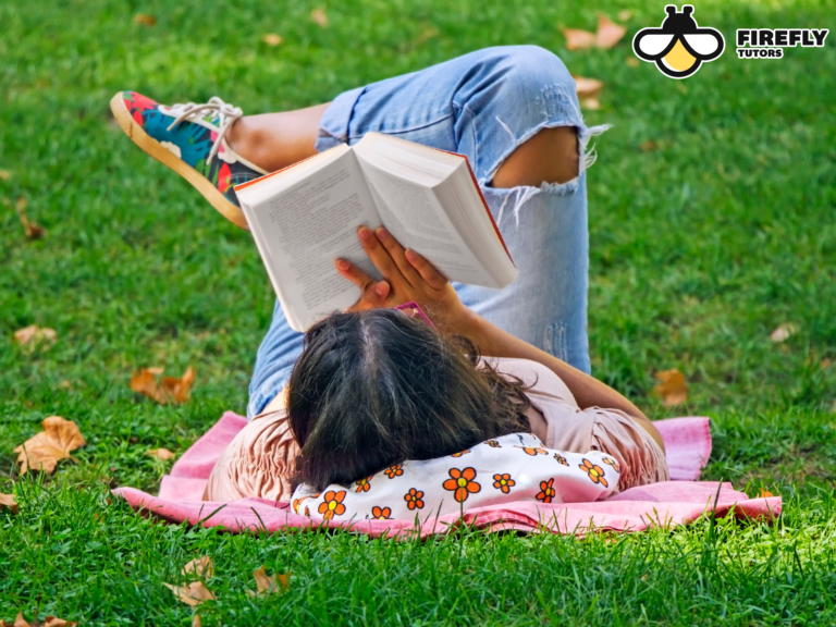 Girl relaxing on a blanket in the grass reading a book on a summer afternoon